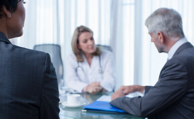 Female doctor, man and woman talking at table in conference room