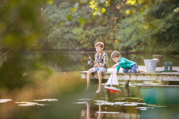 Boys fishing and playing with toy sailboat at lake