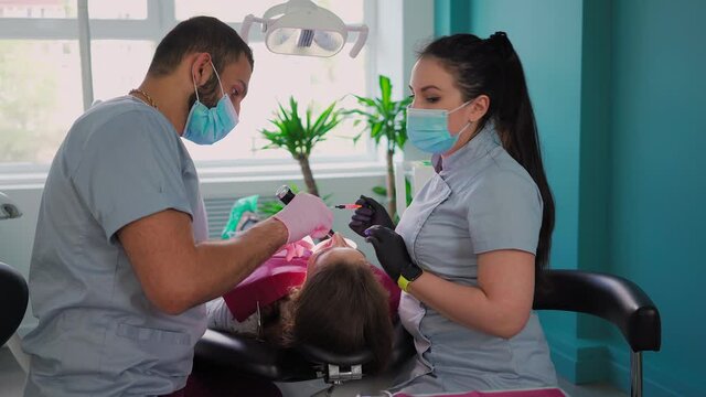 Two doctors, man and woman in protective masks in a dental clinic, serve the patient girl. Work Dentist. Healthcare and medicine concept. Steadicam shooting