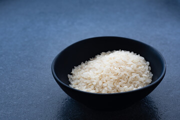 Uncooked rice in black bowl on dark background with copy space