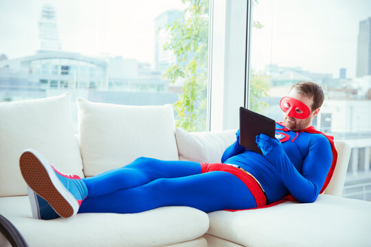 Superhero using digital tablet on living room sofa