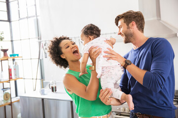 Obraz premium Happy parents holding their baby daughter in domestic kitchen