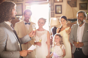Best man toasting champagne giving speech during wedding reception in domestic room - obrazy, fototapety, plakaty