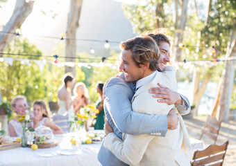 Bridegroom best man embracing during wedding reception in domestic garden