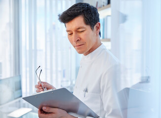 View of man in laboratory holding glasses and chart, looking away