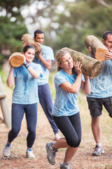 Determined people running with logs on boot camp obstacle course