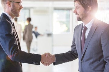 Businessmen wearing suits shaking hands in office, colleagues 