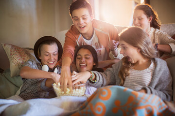 Group of teenagers eating popcorn on sofa in living room