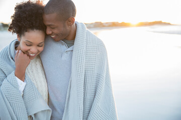 Portrait of couple wrapped in blanket on beach - Powered by Adobe