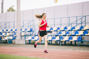 Fototapeta premium Woman Running At Stadium. Young woman running during on stadium track. Goal achievement concept. Fitness Jogging Workout on ballpark. Wellness theme. Sporty training cardio for weight loss success