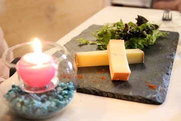 Two pieces of Comté cheese accompanied by salad on a slate plate sprinkled with spices