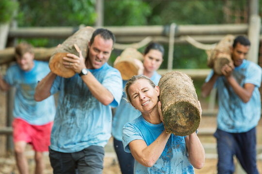 Determined people running with logs on boot camp obstacle course