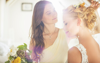 Bridesmaid helping bride with hairstyle in bedroom