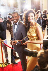 Smiling celebrity couple being photographed by paparazzi photographers at red carpet event