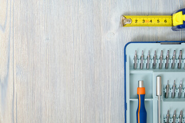 Screwdriver with interchangeable nozzles and tape measure with meter on a wooden gray background with copy space, top view. - Powered by Adobe