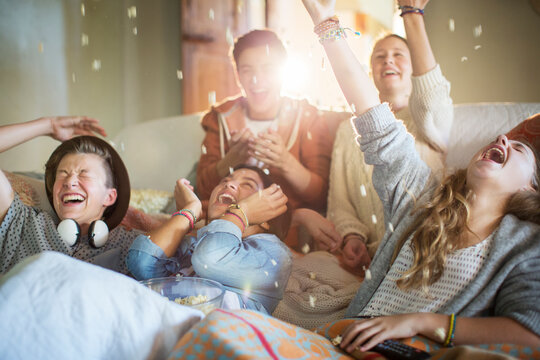 Group of teenagers throwing popcorn on themselves on sofa