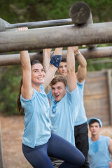 Smiling woman crossing monkey bars on boot camp obstacle course