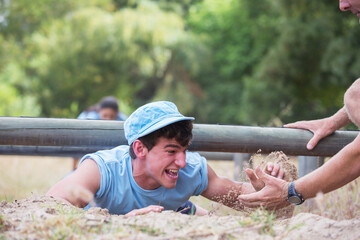 Teammate helping man crawling on boot camp obstacle course