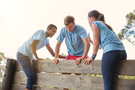 Teammates helping man over wall on boot camp obstacle course - Powered by Adobe