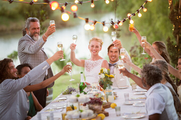 Young couple their guests toasting champagne during wedding reception in garden - obrazy, fototapety, plakaty