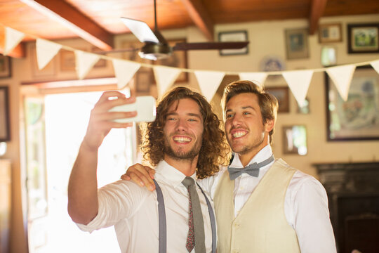 Bridegroom and best man photographing self in domestic room