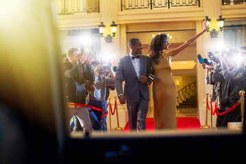 Celebrity couple leaving red carpet event waving to paparazzi photographers - obrazy, fototapety, plakaty
