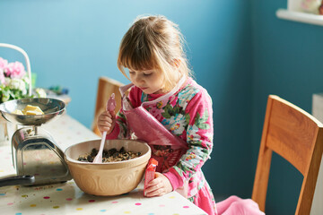 Curious girl baking with mixing bowl in kitchen