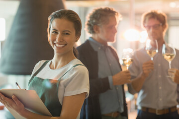 Portrait smiling woman with clipboard working in wine tasting room