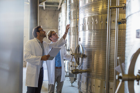 Vintners in lab coats checking vats in winery cellar