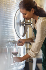 Vintner barrel tasting red wine in stainless steel vat