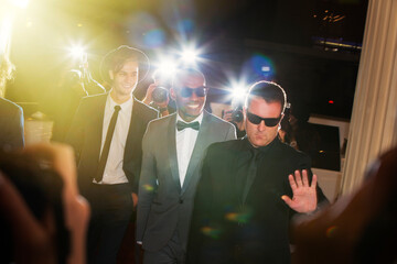 Bodyguard escorting celebrities arriving at event being photographed by paparazzi