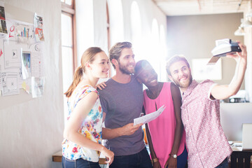 Creative business people taking selfie with instant camera in office