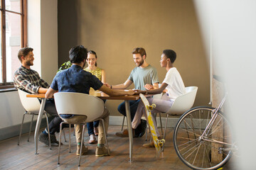 Creative business people holding hands at table in meeting