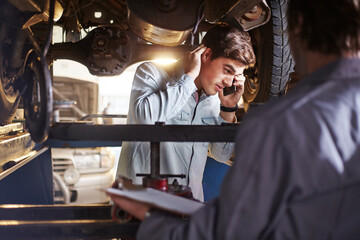 Mechanic and customer talking on cell phone under car