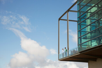 Fototapeta na wymiar Men talking on balcony of glass bump out against blue sky