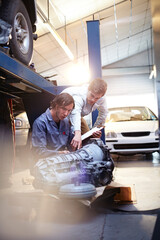 Mechanic and customer examining engine part in auto repair shop