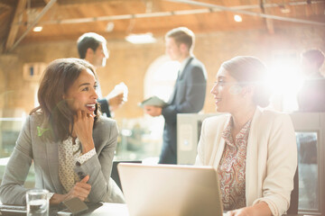 Businesswomen talking and working at laptop in office