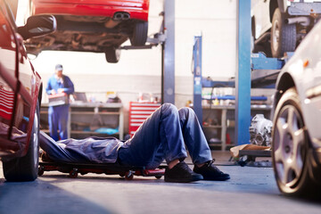 Mechanic under car in auto repair shop - obrazy, fototapety, plakaty