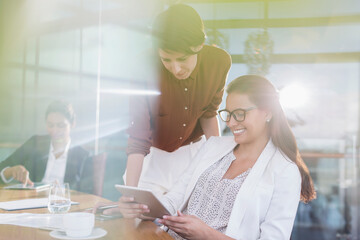 Businesswomen using digital tablet in sunny conference room