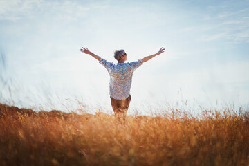 Exuberant senior woman with arms outstretched in sunny field - obrazy, fototapety, plakaty