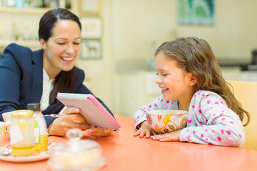 Mother and daughter using digital tablet at breakfast table