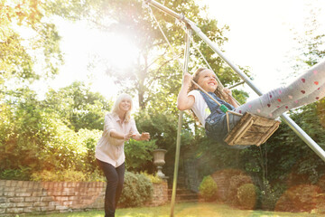 Grandmother pushing granddaughter on swing in backyard