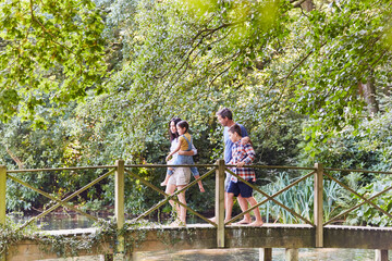 Fototapeta na wymiar Family crossing footbridge in park with trees