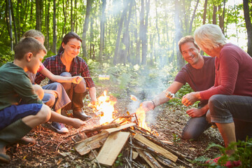 Multi-generation family roasting marshmallows at campfire in forest