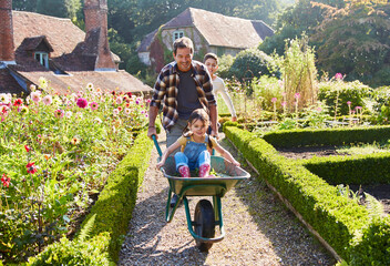 Father pushing daughter in wheelbarrow in sunny garden