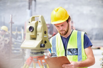 Engineer with clipboard behind theodolite at construction site