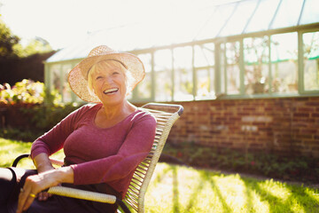 Portrait enthusiastic senior woman sitting outside sunny greenhouse - obrazy, fototapety, plakaty