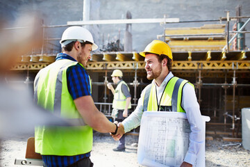 Construction worker engineer blueprints handshaking at construction site - obrazy, fototapety, plakaty