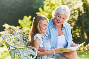 Grandmother reading with granddaughter on garden bench