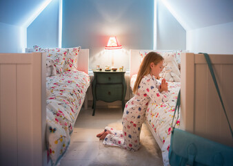 Girl in pajamas saying bedtime prayers at bed